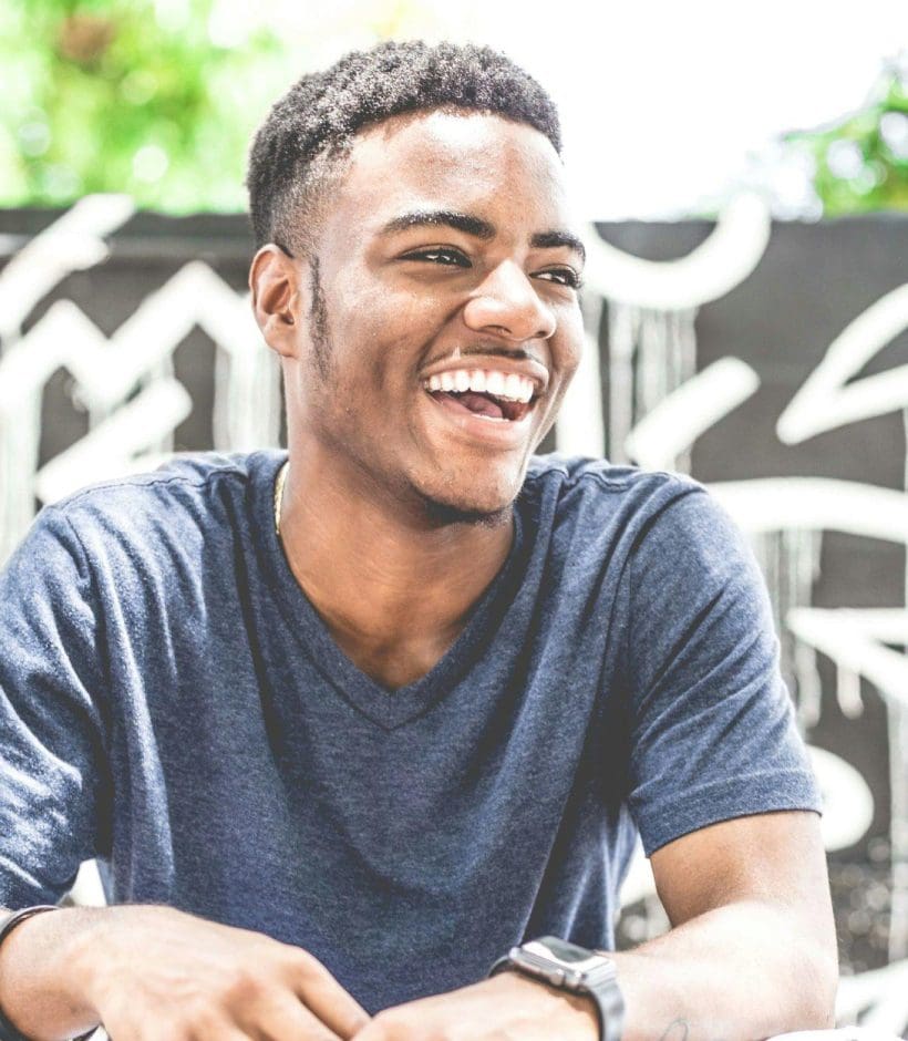 A young man smiling while sitting at an outdoor table.