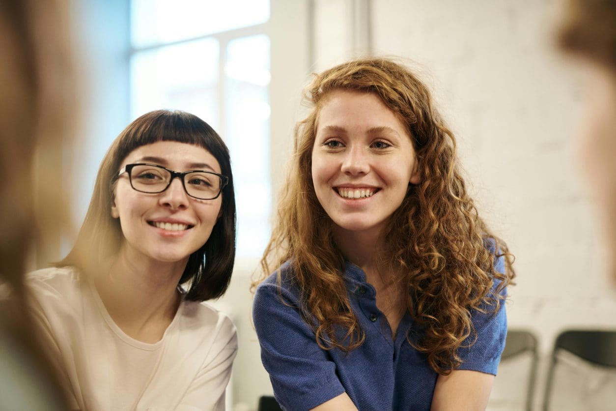 Two women smiling for a picture in front of a window.