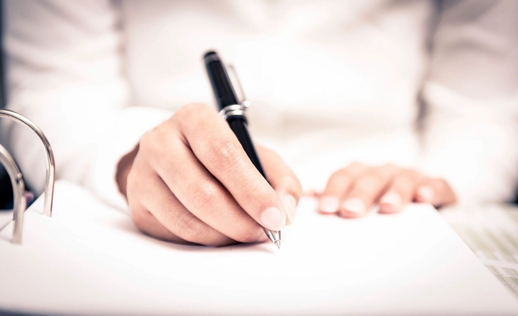 A person writing on paper with a pen.